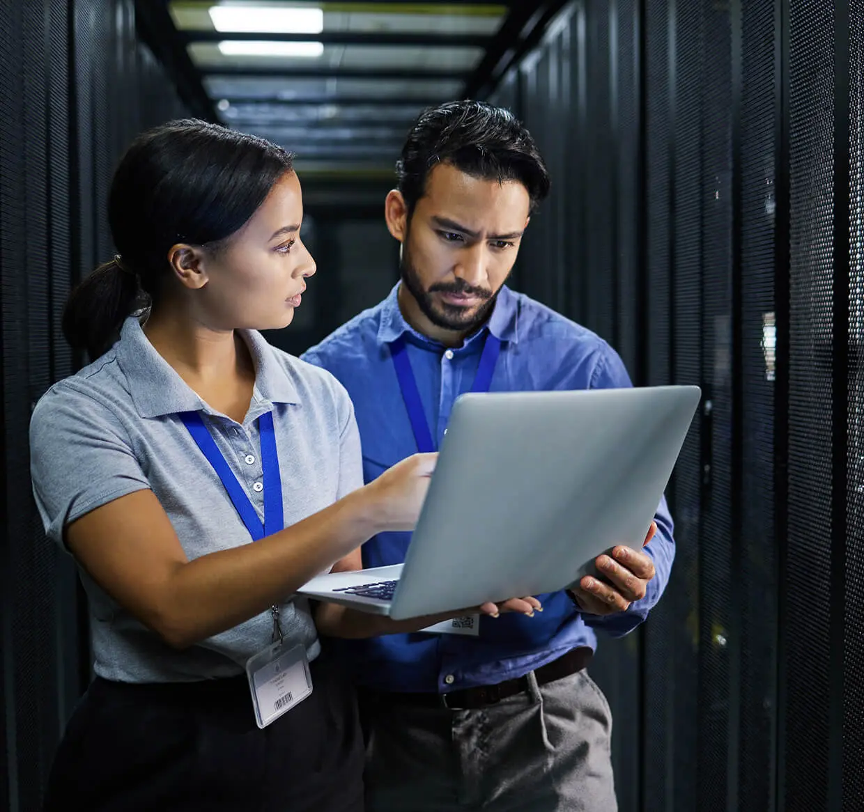 Two people examining laptop in server room.